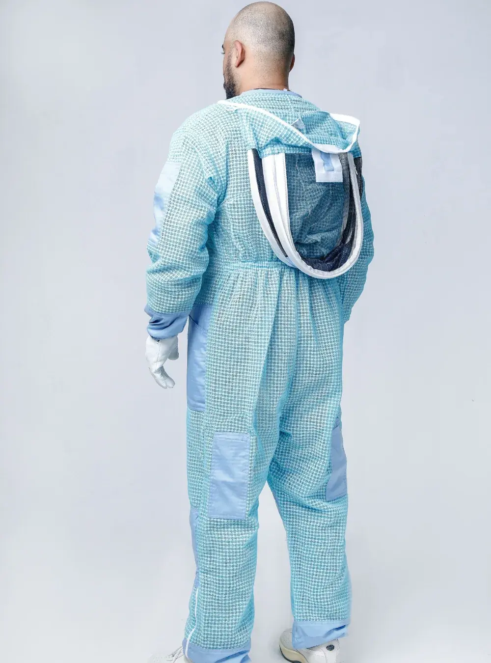 Three-quarter back view of a beekeeper in a blue ventilated suit with the fencing veil folded back