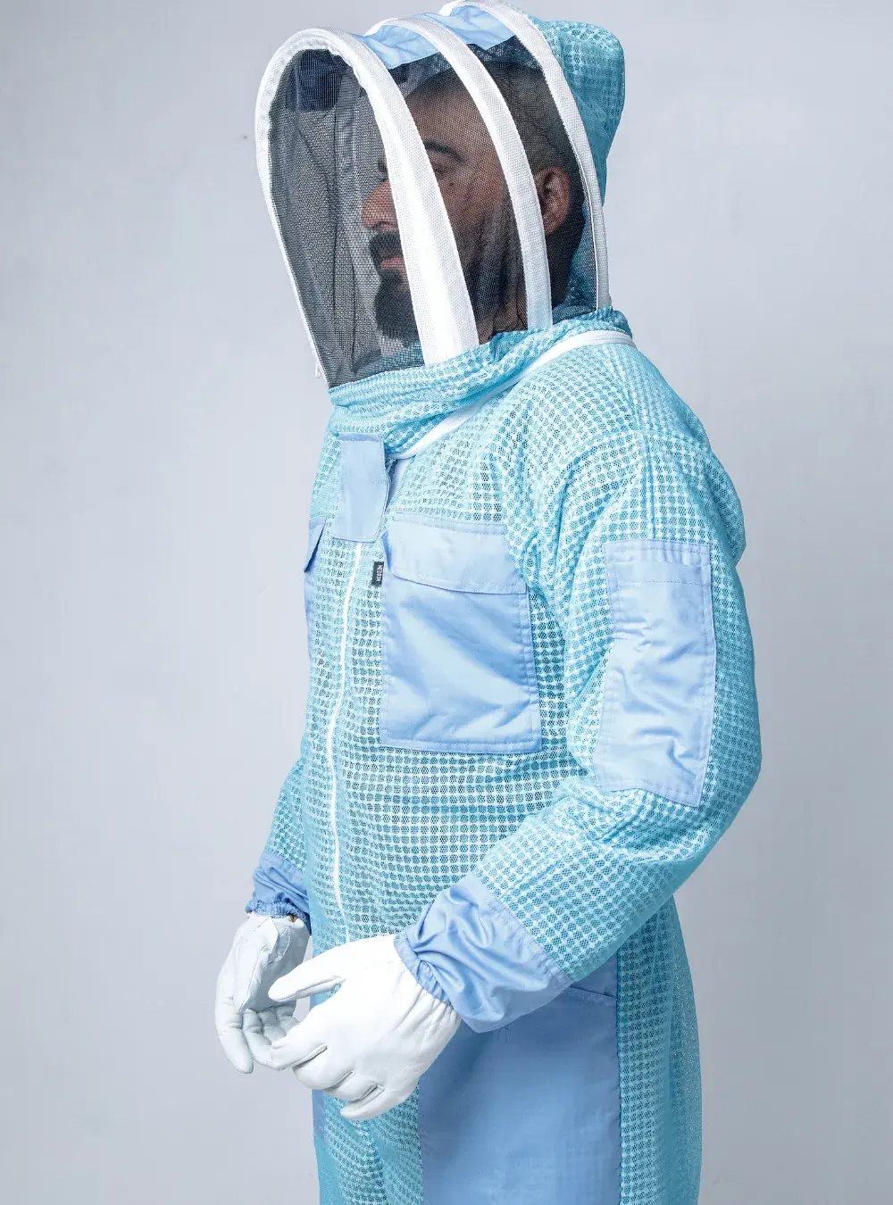 Side view of a beekeeper in a blue ventilated suit with the fencing veil up and the arms bent, showing sleeve length to the gloves